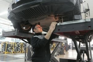 Mechanic inspecting car on lift in an automotive garage, focusing on vehicle repair and maintenance.