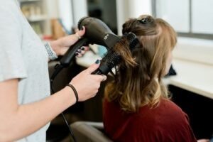A hairstylist using a blow dryer and round brush on a client's hair